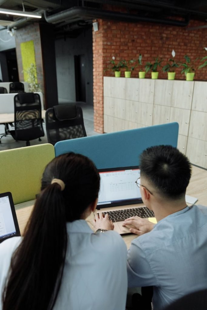 a-man-and-a-woman-using-a-laptop-7653573 Two colleagues collaborating on a laptop in a modern, open-plan office space.