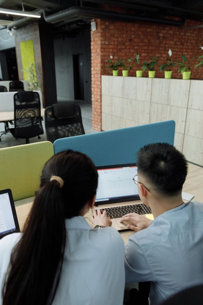 Two colleagues collaborating on a laptop in a modern, open-plan office space.
