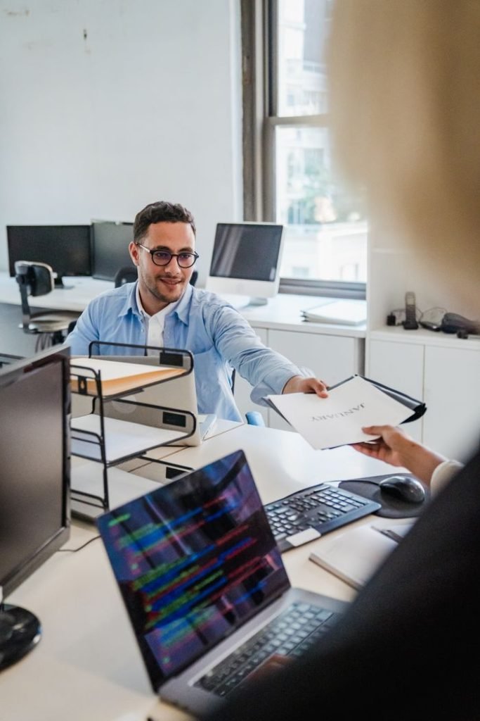 businessman-working-in-an-office-12902868 Two office workers exchanging documents in a bright office setting.